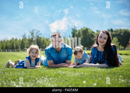 Famiglia allegra in un parco, i genitori e i loro due bambini sono sdraiati sull'erba. Girato con flare Foto Stock