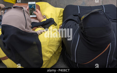 Trainare le donne musulmane seduta su una panchina in Trafalgar Square con occhiali da sole sulla parte superiore della loro il velo o abiti di testa utilizzando il telefono cellulare. la tradizione. Foto Stock