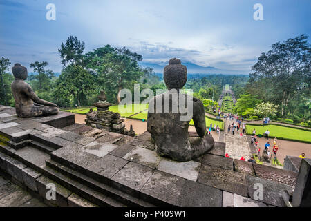 Un sereno Budda seduto orologi come visitatore folla mak il loro modo al salire del IX secolo tempio Buddhista di Borobudur e Java centrale, Indonesia Foto Stock