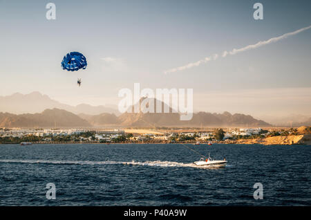 Il parasailing in cielo vicino alla spiaggia trainato da barca a motore al tramonto. Sharm el Sheikh, Mar Rosso, Sinai, Egitto Foto Stock