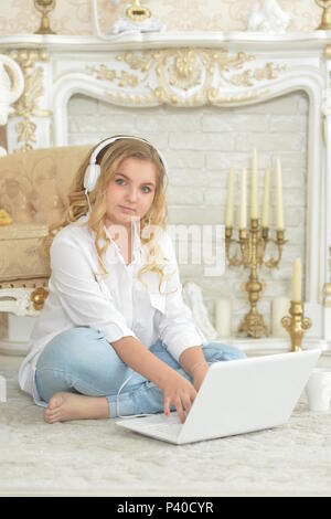 Curly blonde ragazza adolescente nelle cuffie seduto sul pavimento Foto Stock