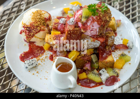 Piatto da dessert di miele toast con gelato vaniglia, mista fresca frutta affettata, fette di mango, kiwi, dragon frutta e panna montata su tavolo in metallo Foto Stock