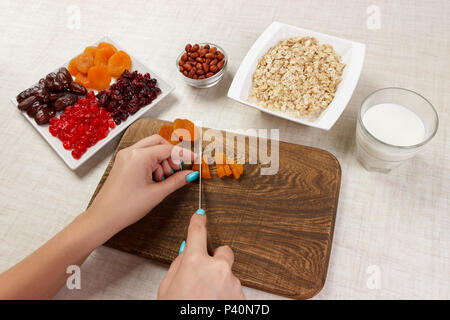 La ragazza si sta preparando la sua prima colazione. Il taglio della frutta secca in fiocchi d'avena porridge su un tagliere. Utile e salutare prima colazione. sfondo luminoso. Foto Stock
