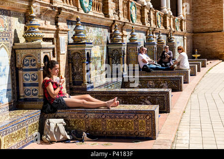 I turisti di relax al sole sulla provincia piastrellato alcove, Plaza de Espana, Andalusia, Spagna. Foto Stock