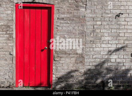 Chiusa la porta di legno di colore rosso brillante su un muro di mattoni Foto Stock