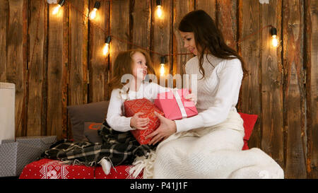 Madre e un simpatico bambina agitando Xmas presenta e cercando di indovinare che cosa è interno Foto Stock