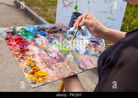 Un close-up artist pitture su tela un paesaggio urbano di un argine di estate con le attrazioni di vernici a olio Foto Stock