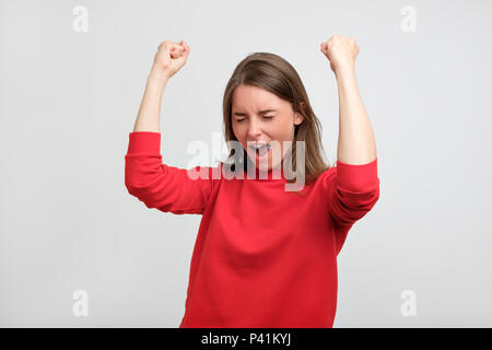 Felice caucasian woman in red maglione esulta pugni di pompaggio celebra il successo o la vittoria del suo calcio teamShe ha superato l'esame o ricevere nuovo lavoro Foto Stock