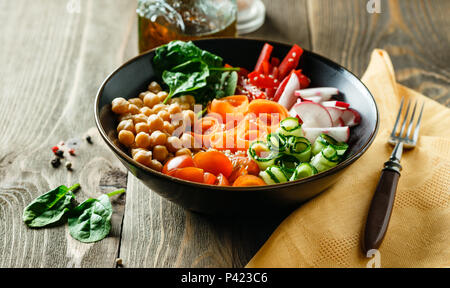 Buddha colorato ciotola con ceci, carote, pomodori, cetrioli, radicchio e peperoni su di un tavolo di legno. Insalata vegetariana. Foto Stock