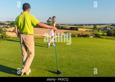 L'uomo guarda il suo partner che colpisce la palla durante la partita sul campo da golf Foto Stock