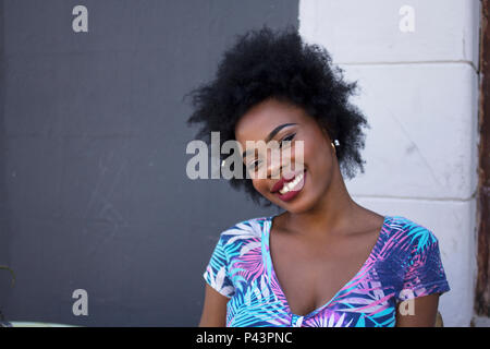 Un africano modello femminile pone al fianco di un oscuramente contrastato la parete Foto Stock