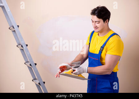 Giovane dipendente del contraente di applicare gesso sulla parete Foto Stock