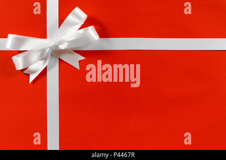 Bordo di Natale regalo telaio nastro in raso bianco su carta rossa orizzontale di sfondo Foto Stock