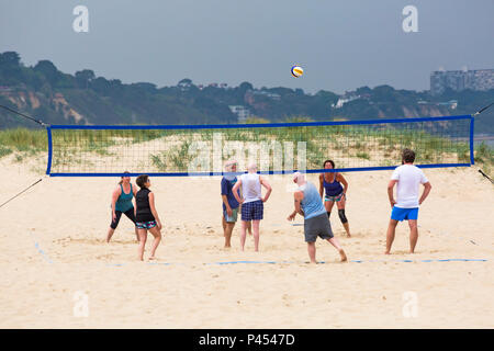 Le persone aventi divertirsi giocando a pallavolo in spiaggia a banchi di sabbia spiaggia sotto il grigio scuro cielo tempestoso, Poole, Dorset nel Maggio Foto Stock