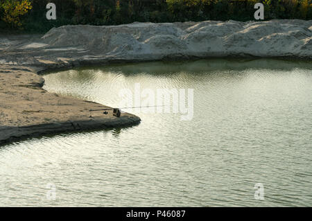 La pesca dal capo della costa sabbiosa. Dune di sabbia circondano la lussureggiante vegetazione.ombre vaghe di alberi e la costa. Piccole onde sulla superficie disrup. Foto Stock