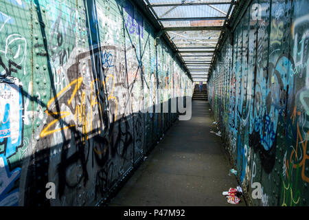 Persona in la distanza di avvicinamento ponte pedonale con ciascuna parete coperto di graffiti e rifiuti sul suolo, Sheffield, England, Regno Unito Foto Stock