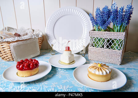 Torte su piastre stare accanto a una piastra bianca su un piedistallo e cestello e fiori. Foto Stock