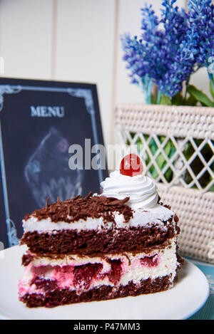 Torta al cioccolato con crema e ciliegia su una piastra bianca. Foto Stock