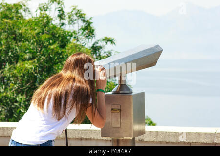 Ragazza giovane guardando attraverso il binocolo pubblico in riva al mare Foto Stock