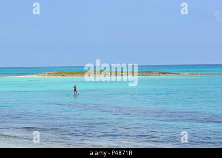 Uomo in lontananza su paddleboard nelle acque blu colorate delle Bahamas Foto Stock
