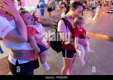 Due le mamme con bambini in vettori torace godetevi la vita notturna al city square sulla calda serata estiva, Libo, Guizhou, Cina. Foto Stock