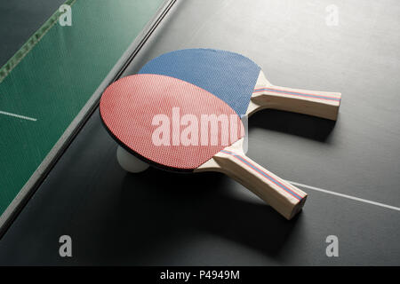 Ping Pong pagaie posa su un tavolo da ping pong con la rete mostra, entrambe le palette sullo stesso lato con illuminazione difficili Foto Stock