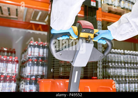 Lavoratore di stoccaggio spingendo la maniglia del carrello per movimentazione pallet Foto Stock