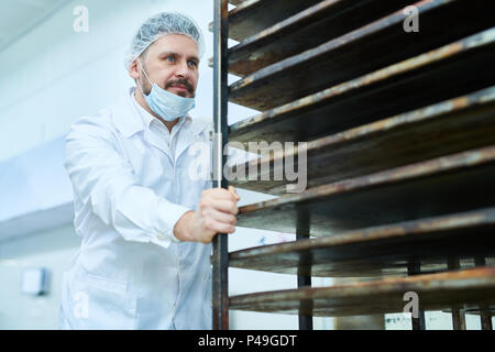 Uomo in bianco uniforme ripiani mobili per il pane Foto Stock