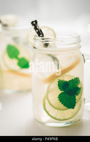 Freschi cocktail mojito con il ghiaccio freddo, limone e foglie di menta in Mason Jar sul legno bianco come sfondo luminoso il concetto di estate Foto Stock