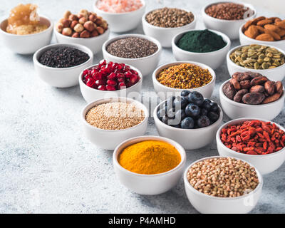 Varie superfoods nella piccola ciotola di cemento grigio Sfondo. Super come chia, spirulina, materie fava di cacao, goji, canapa, quinoa, polline di api, sesamo nero, curcuma. Copia spazio per il testo. Foto Stock