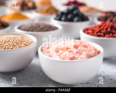 Sale rosa in piccola ciotola bianco e altri superfoods sullo sfondo. Messa a fuoco selettiva. Superfoods diversi ingredienti. Concetto e illustrazione per la super e detox food Foto Stock