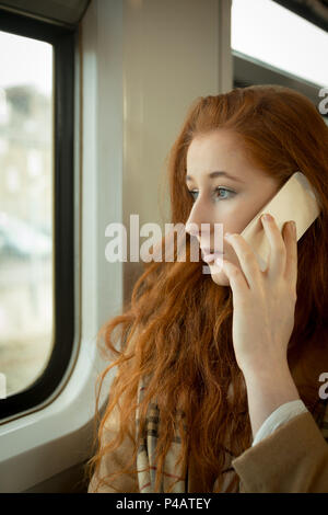Donna che parla al telefono cellulare mentre si è in viaggio in treno Foto Stock