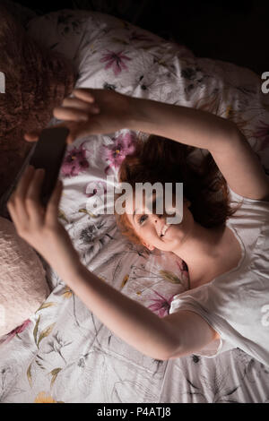 Donna prendendo selfie con telefono cellulare in camera da letto Foto Stock