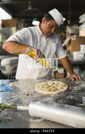 Voce maschile baker versando olio su un impasto Foto Stock