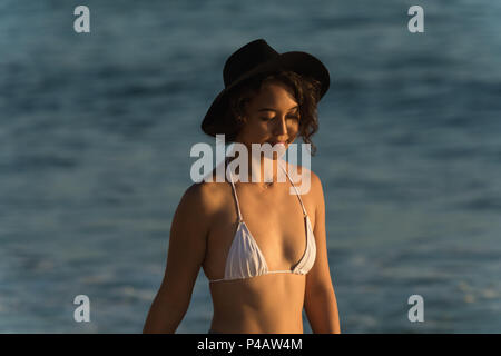 Donna in piedi in spiaggia al tramonto Foto Stock