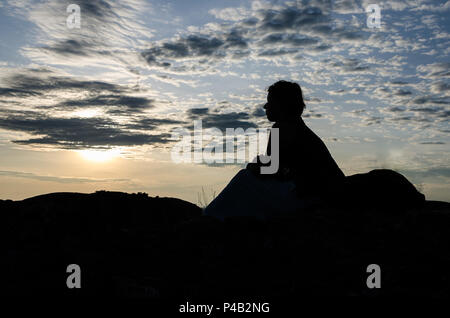 Silhouette di giovane donna seduta sulla parte superiore delle rocce di Pedras Negras o Pundo Andongo durante il tramonto con cielo drammatico, Angola, Africa. Foto Stock