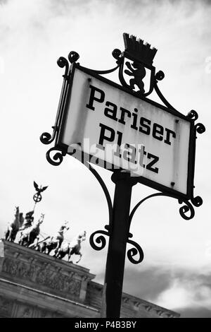 Primo piano di una targa in strada con il nome ot Pariser Platz a Berlino, Germania, con la Porta di Brandeburgo in background, in bianco e nero e Foto Stock
