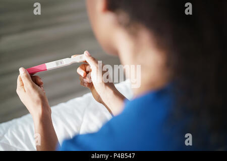 Premuto giovane donna ispanica con ansia sensazioni sul letto. Black girl holding negative al test di gravidanza. Close-up di mani e kit Foto Stock