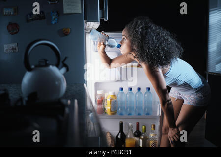 Giovane africano donna americana la sofferenza per il calore estivo e la mancanza di aria condizionata a casa. Nero Ragazza coperto con il sudore di bere acqua fresca da f Foto Stock