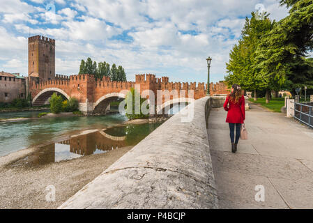 Donna che cammina sul lungofiume di Verona. Castelvecchio bridge in background. Verona, Veneto, Italia Foto Stock