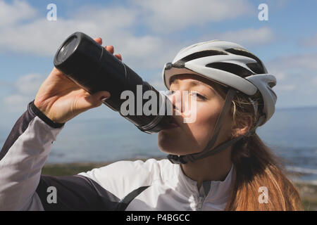 Biker femmina acqua potabile dalla bottiglia su un soleggiato Foto Stock