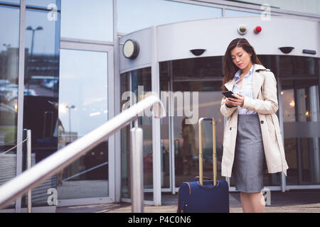 Imprenditrice utilizzando il telefono cellulare al di fuori di un hotel Foto Stock