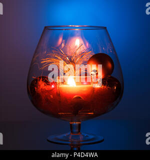 Una candela che brucia in un vaso di vetro, decorazione e vari elementi di Natale su uno sfondo blu scuro. Foto Stock