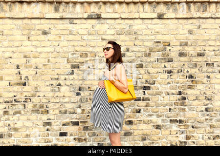 La gravidanza e la maternità e felice futuro concetto madre - donna incinta a city tour contro un muro di mattoni Foto Stock