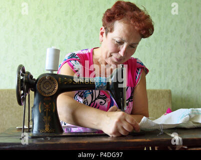 Jartsevo, Russia - Luglio 28, 2014: Una donna anziana cuce su un lato della macchina per cucire 'Singer' Foto Stock