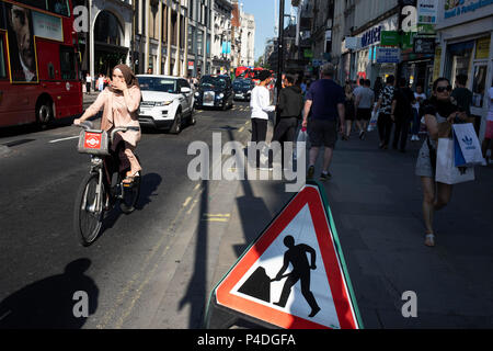 Scena occupato su Oxford Street come ciclo di persone passato a uomini al lavoro sign in London, England, Regno Unito. Foto Stock