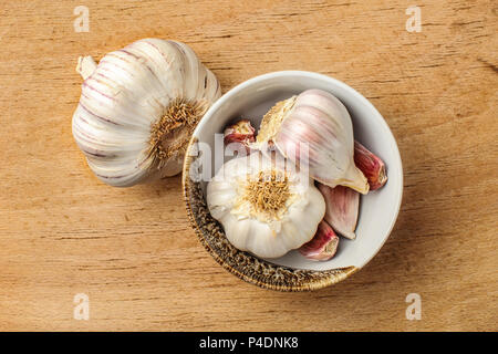 Tabella vista dall'alto sui bulbi di aglio e chiodi di garofano in piccolo vaso in ceramica, posto sul vecchio tagliere di legno. Foto Stock