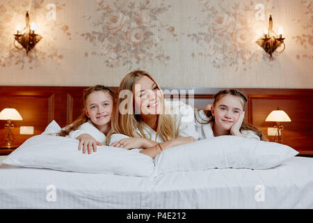 Ritratto di un ridere la madre ed i suoi figli gemelli giacente su un letto in una camera accogliente. Foto Stock