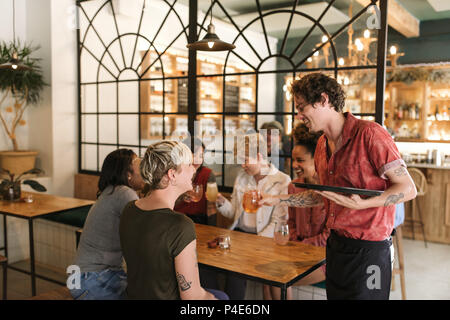 Variegato gruppo di amiche ordinare bibite da un bistrot cameriere Foto Stock