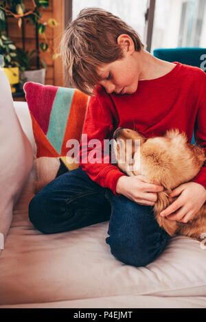 Ragazzo seduto sul divano abbracciando il suo golden retriever cane Foto Stock